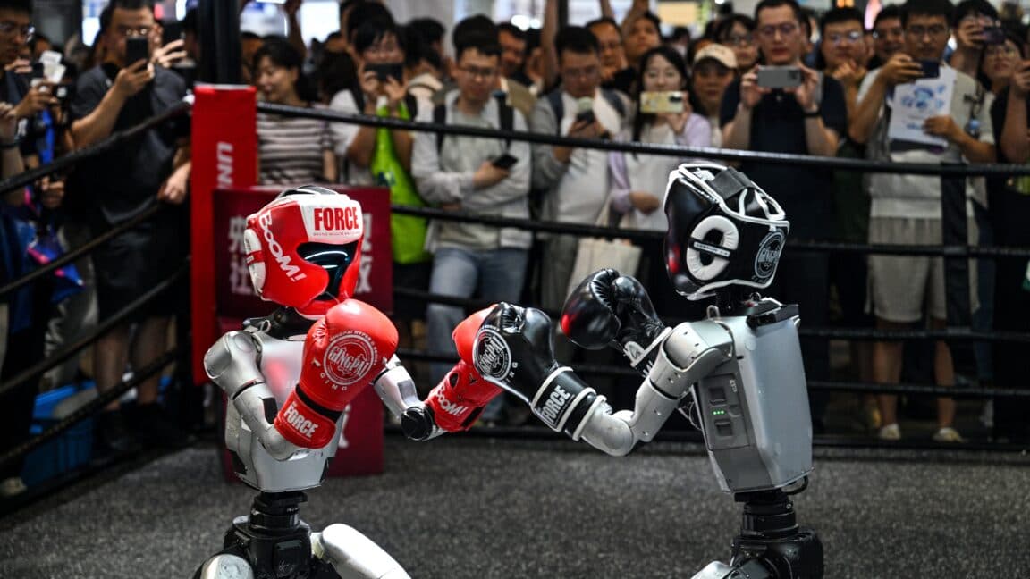 A humanoid robot standing next to a robot vacuum cleaner in a modern home setting