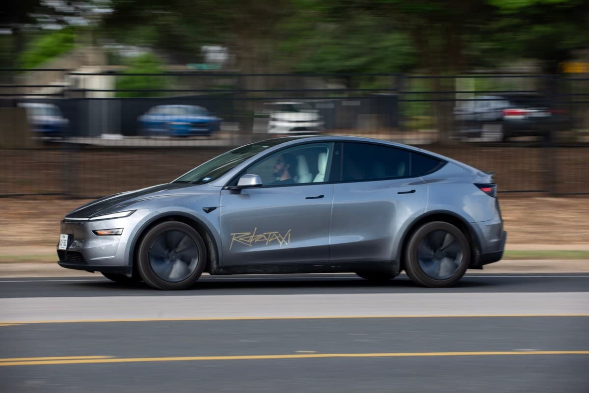 A Tesla vehicle driving on a sunny street in an urban Florida setting, representing robotaxi pilot operations in Orlando and