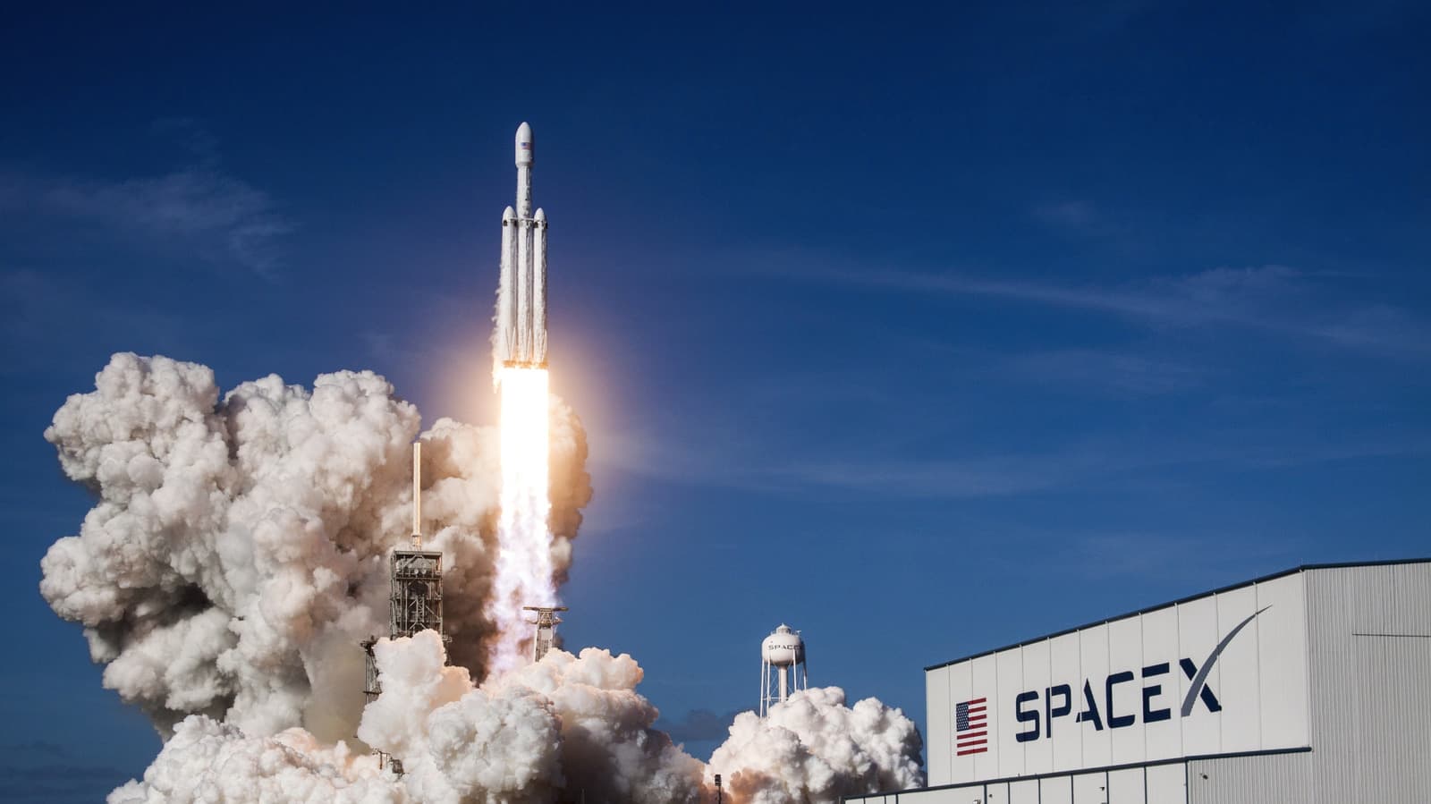 A SpaceX Falcon 9 rocket launching from Cape Canaveral with exhaust plumes against blue sky