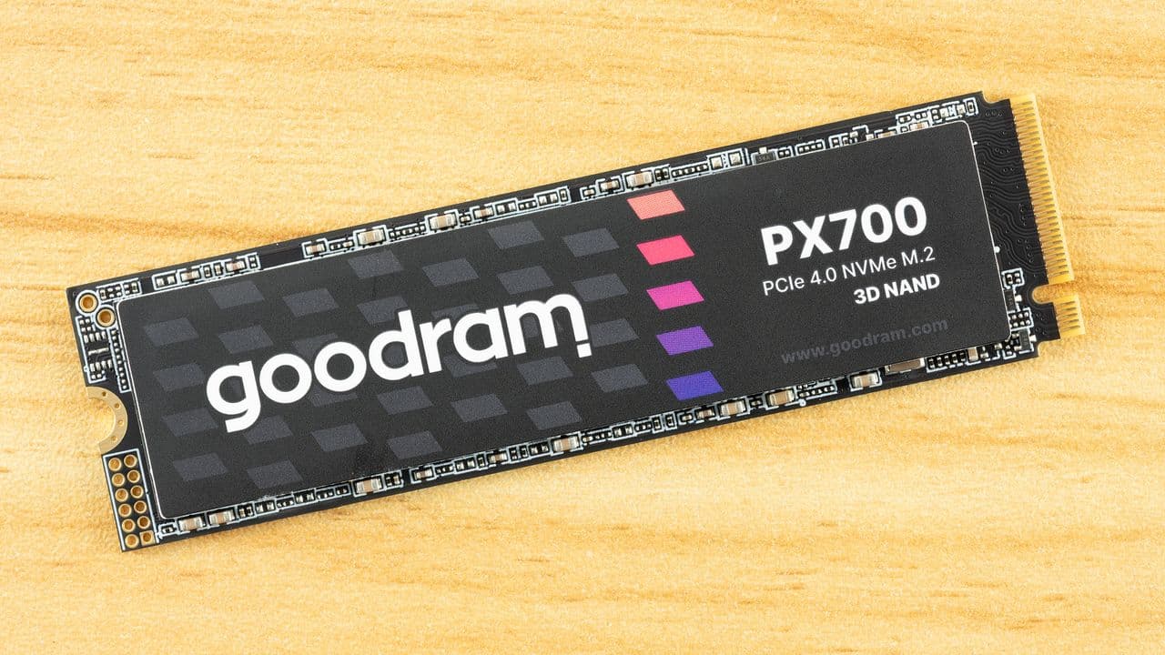 Goodram PX700 2TB SSD on a wooden desk next to a laptop with benchmarking screen visible