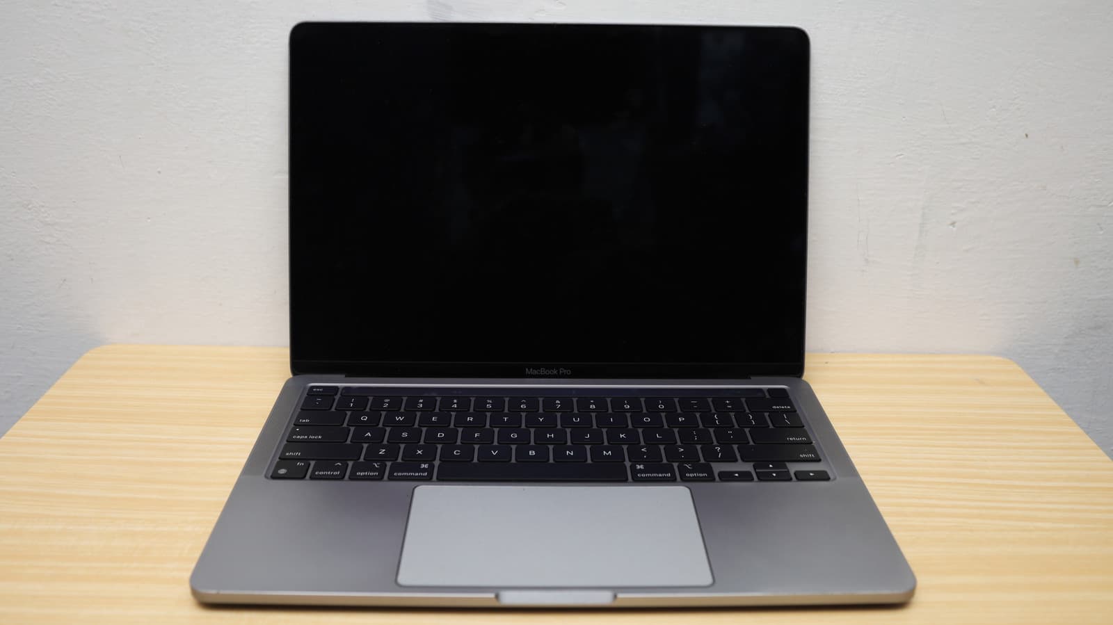 A MacBook laptop with a black screen sitting on a desk, with a troubleshooting guide nearby