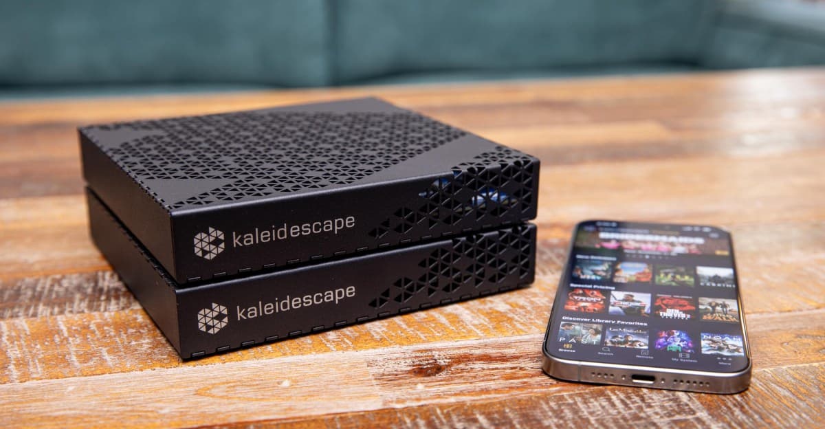 Kaleidescape Strato E movie player and Mini Terra Prime server stacked on a wooden table next to a smartphone displaying the