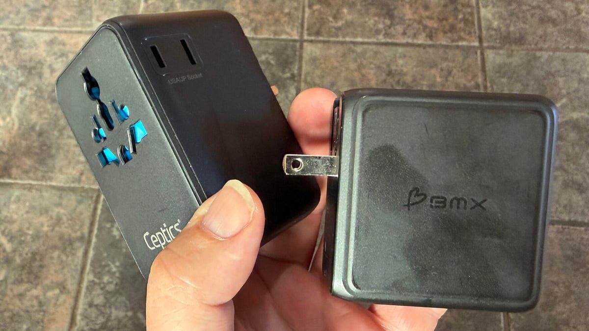 Close-up of a universal adapter plugged into a wall socket next to a travel charger showing USB ports