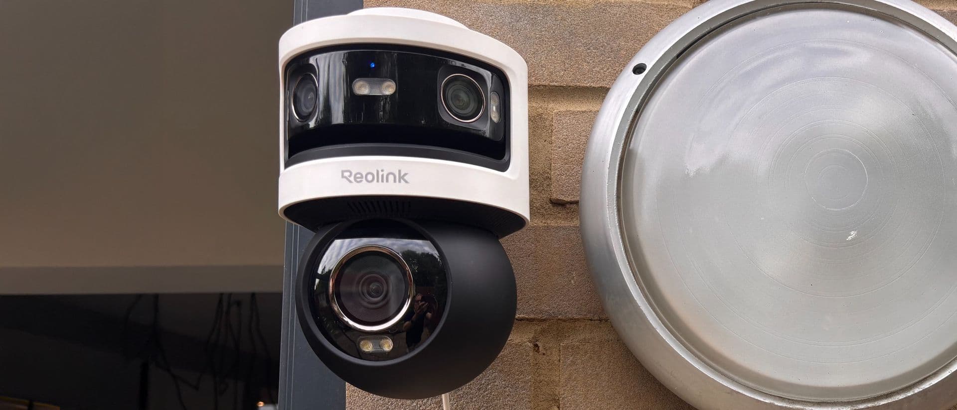 Reolink OMVI 3i security camera mounted on an exterior wall with spotlights illuminating a driveway