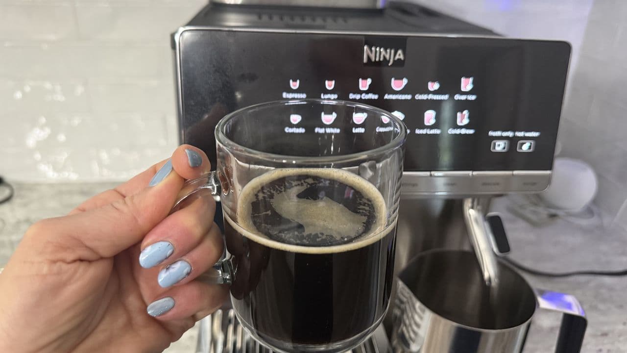 Person using the Ninja AutoBarista Pro coffee machine with whole beans in the hopper, highlighting the Grind iQ feature
