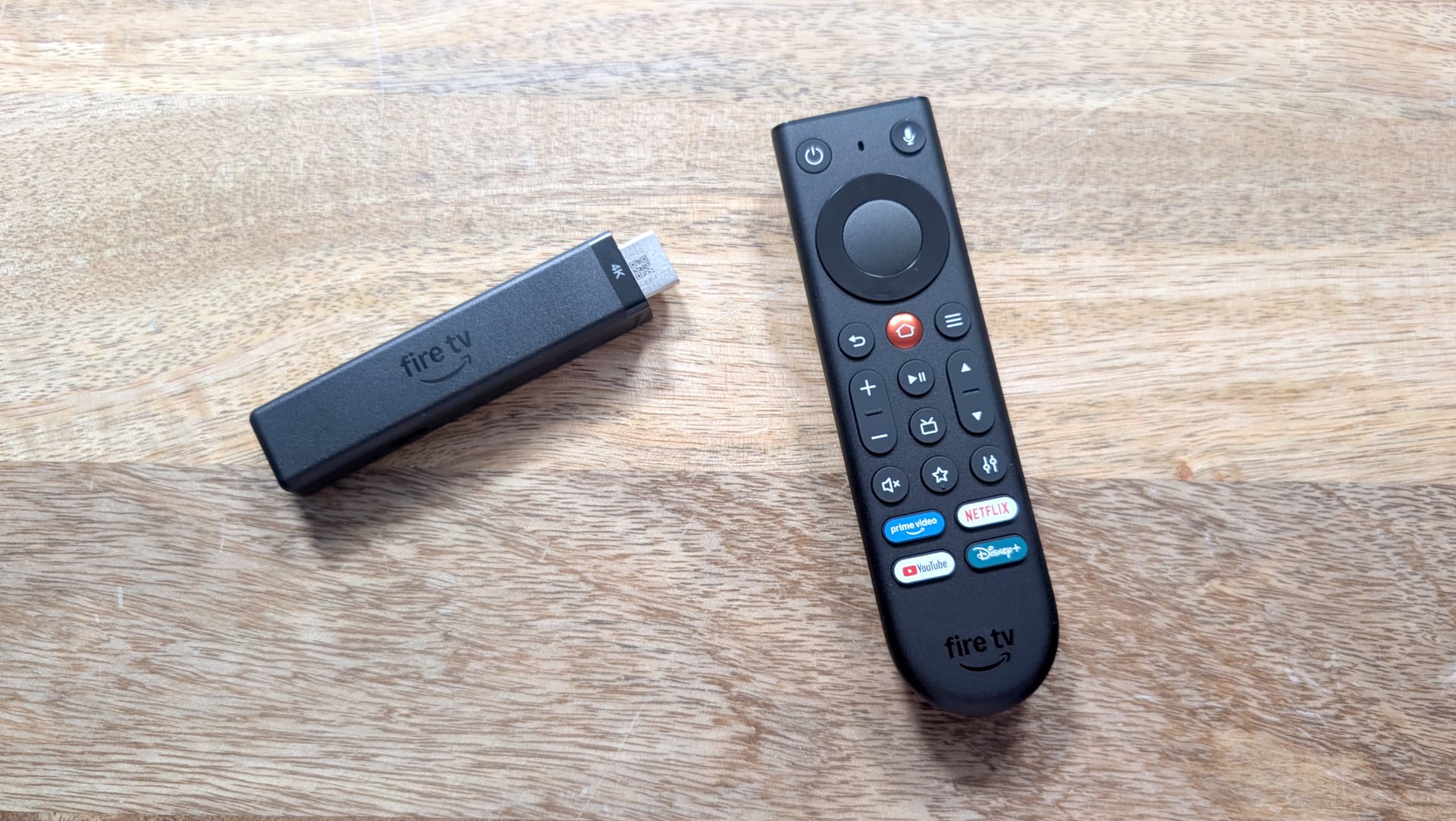 Amazon Fire TV Stick 4K remote and device on a wooden table next to a TV