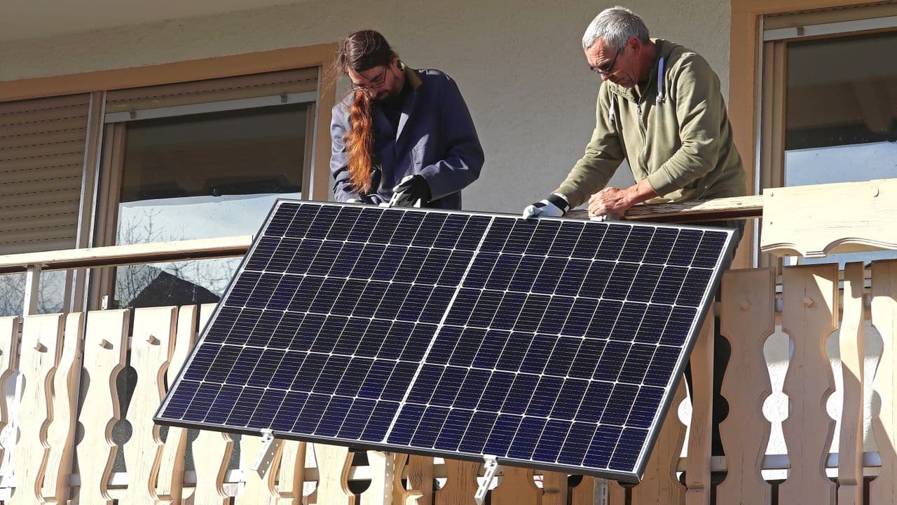 Man and boy standing on a balcony with a solar panel installed, representing plug-in solar adoption in Europe