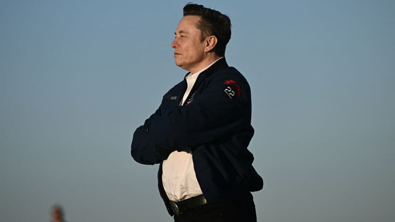 Elon Musk speaking at an event with a data center background, representing AI infrastructure expansion